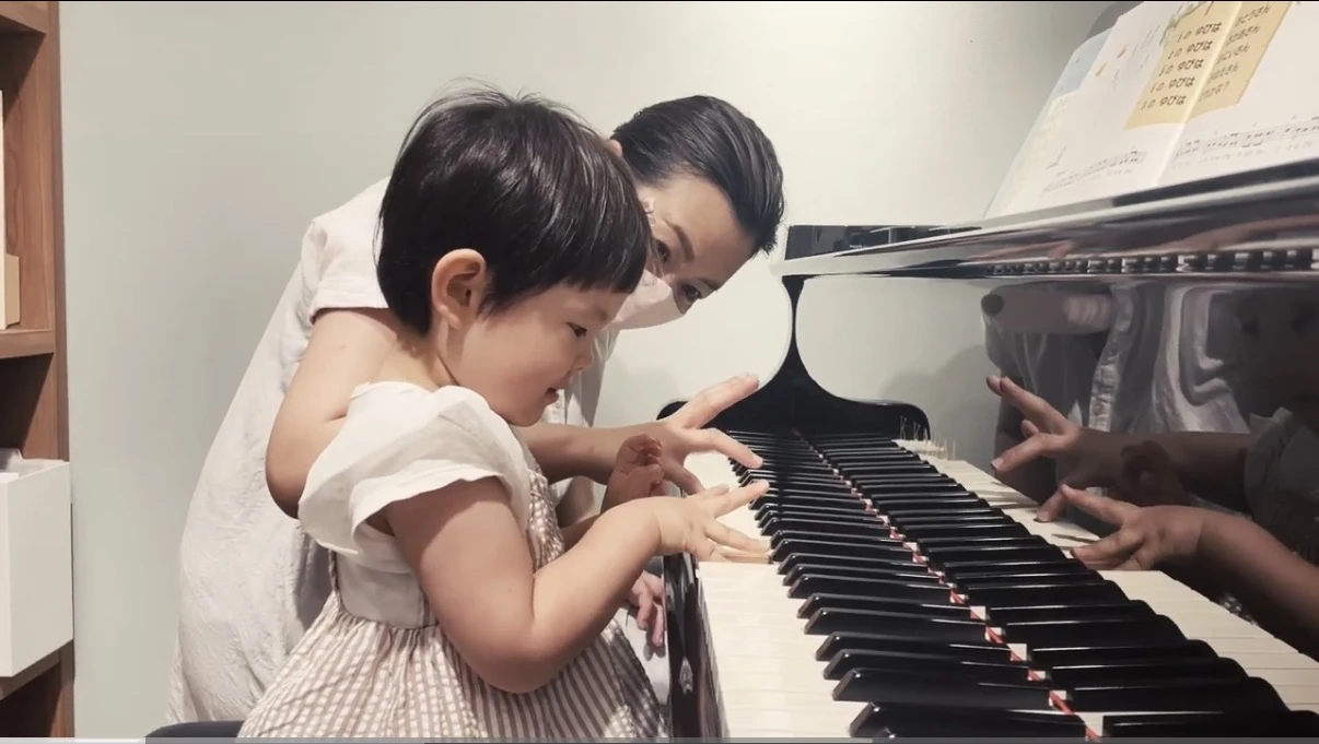 先生に見守られながら、お子さんがグランドピアノの鍵盤に触れるレッスンの様子